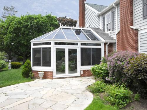 : A conservatory pictured from outside that is attached to a brick home with a stone walkway leading up to it.